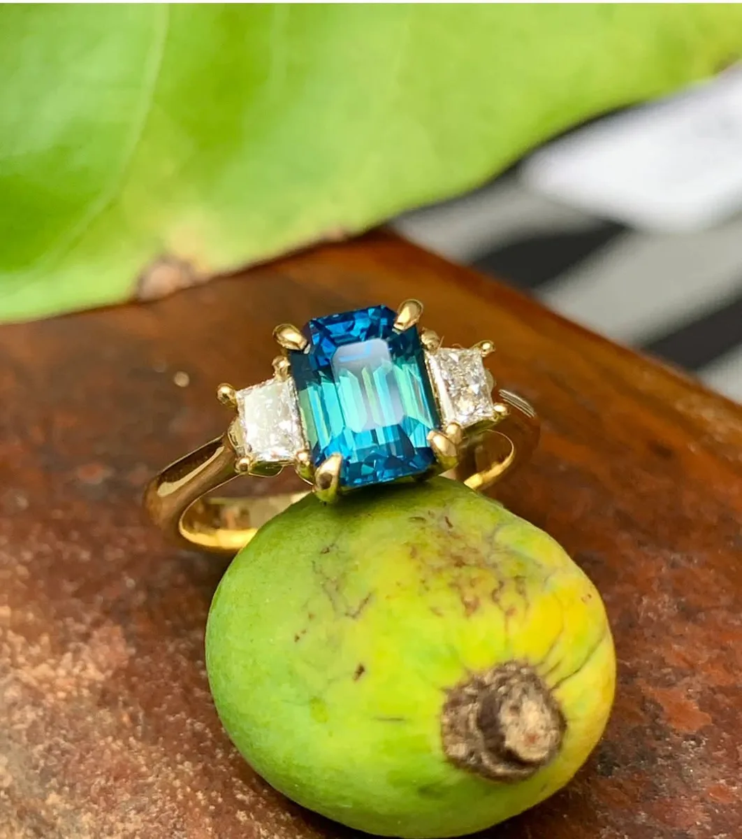 Teal blue emerald-cut sapphire trilogy engagement ring in yellow gold